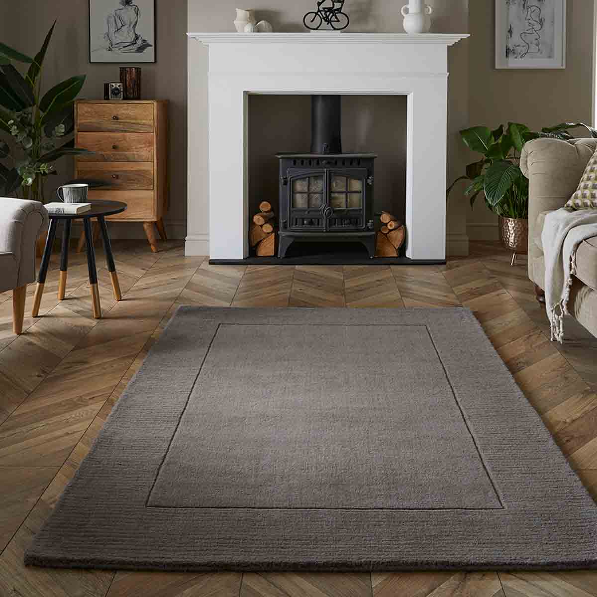 Soft grey wool rug measuring 80x150cm, featuring a simple border design, placed on a herringbone wooden floor in a cozy living room setting.