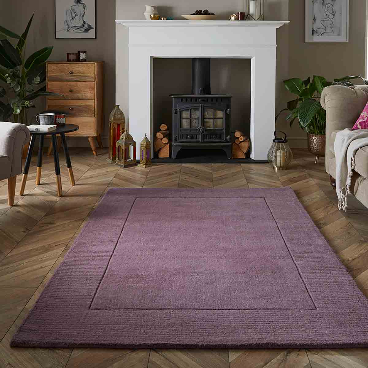Mauve wool rug measuring 120x170cm, featuring a subtle textured design, placed on a herringbone wooden floor in a cozy living room setting.