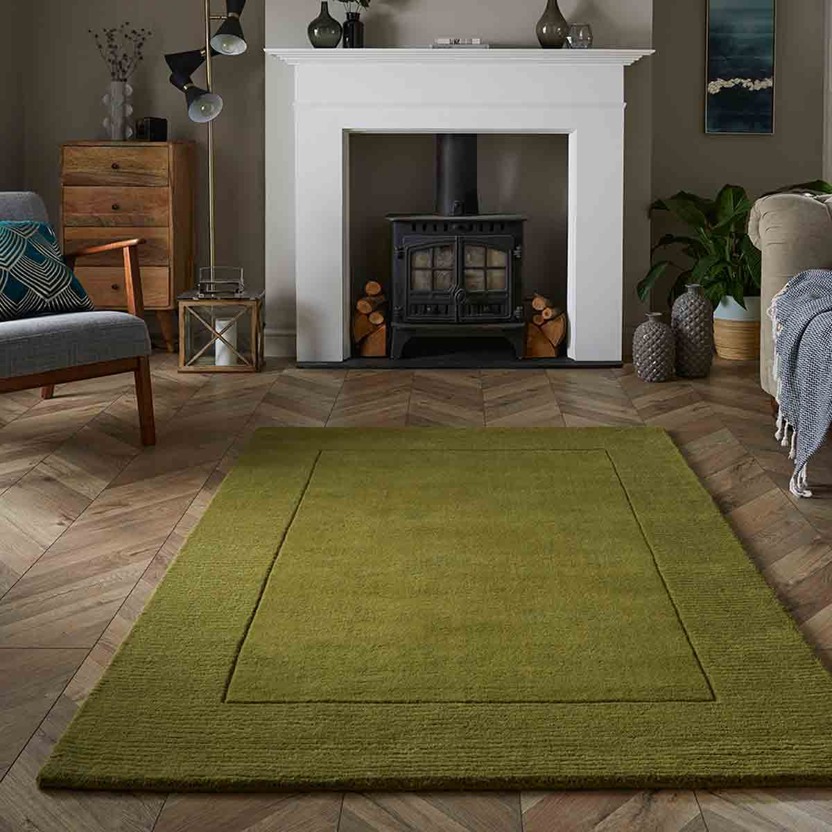 Olive green wool rug measuring 160x230cm, featuring a subtle textured design, placed on a wooden herringbone floor in a cozy living room setting.