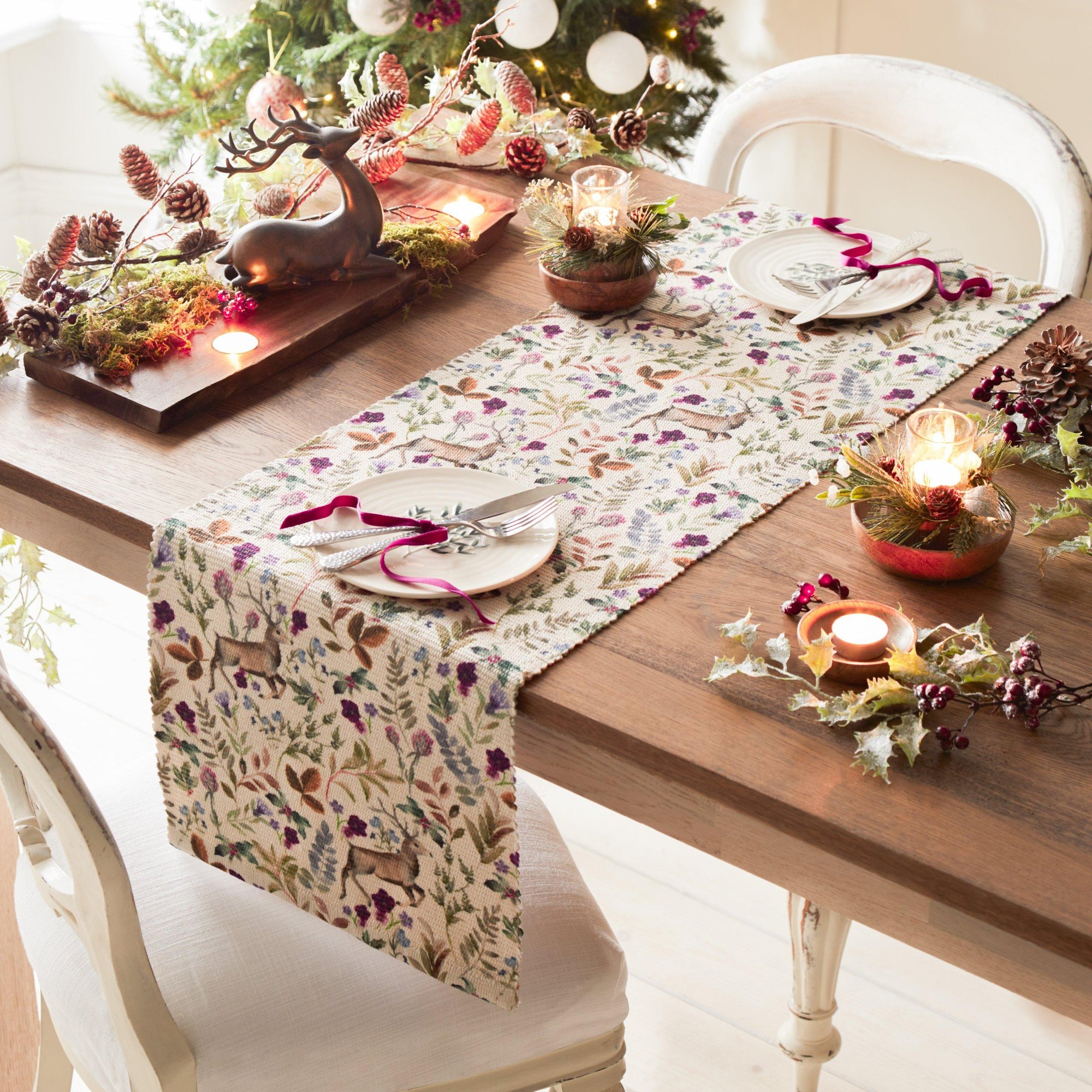 Purple digitally printed table runner featuring reindeer and floral patterns, made of fabric, elegantly placed on a wooden table with festive decorations and candles.