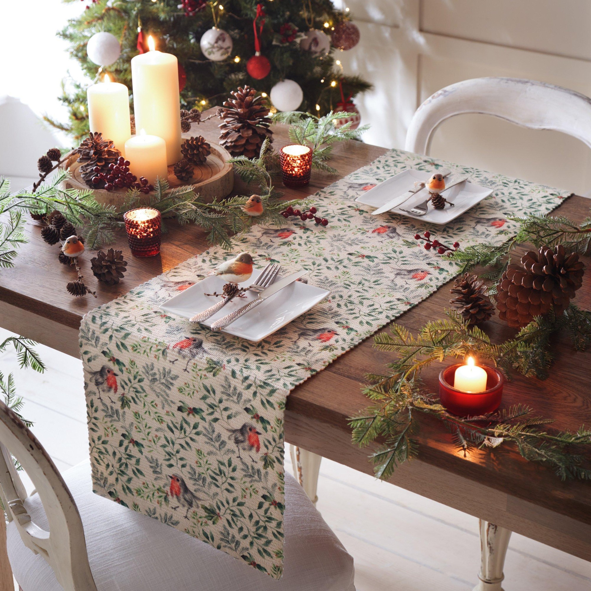 Digitally printed table runner featuring a robin and floral design in soft colors, made of fabric, elegantly placed on a wooden table adorned with candles and pinecones.