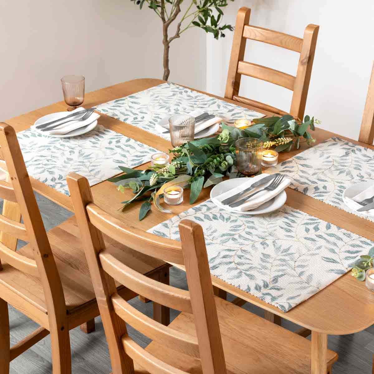 Set of 4 indoor/outdoor placemats featuring a leafy design in soft green and beige tones, made from durable material, arranged on a wooden dining table with plates and candles.