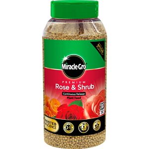 Clear plastic container filled with small, light brown granules, featuring a green and red label with "Miracle-Gro" and "Rose & Shrub" text, alongside images of roses.