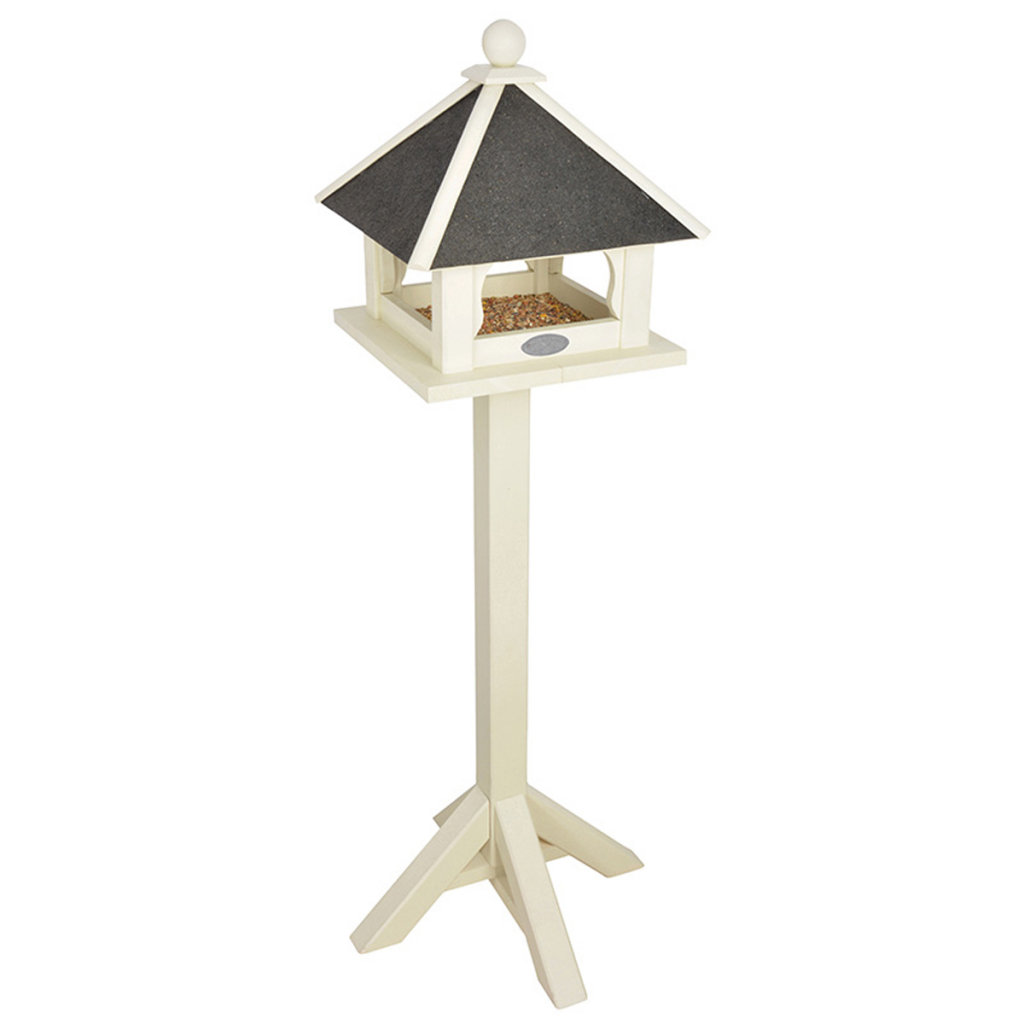 A white wooden birdhouse with a slanted black roof, featuring a square feeding platform and a decorative finial, mounted on a sturdy, four-legged post.
