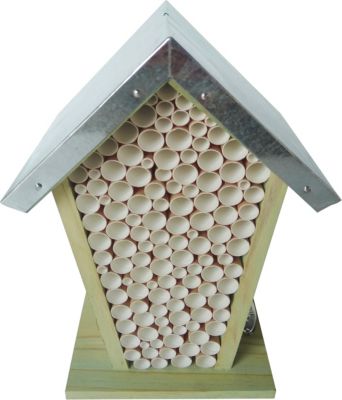 A wooden insect hotel shaped like a house, featuring a sloped metal roof and filled with numerous cylindrical tubes for bees, showcasing natural wood tones and a rustic design.