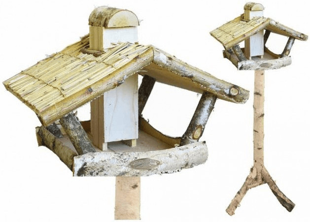 Wooden bird feeder with a thatched roof, featuring a rustic design made from branches and birch wood, mounted on a sturdy wooden post.