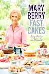 A smiling woman with short blonde hair stands behind a table filled with colorful cakes and pastries, featuring the title "Fast Cakes: Easy Bakes in Minutes" prominently displayed.