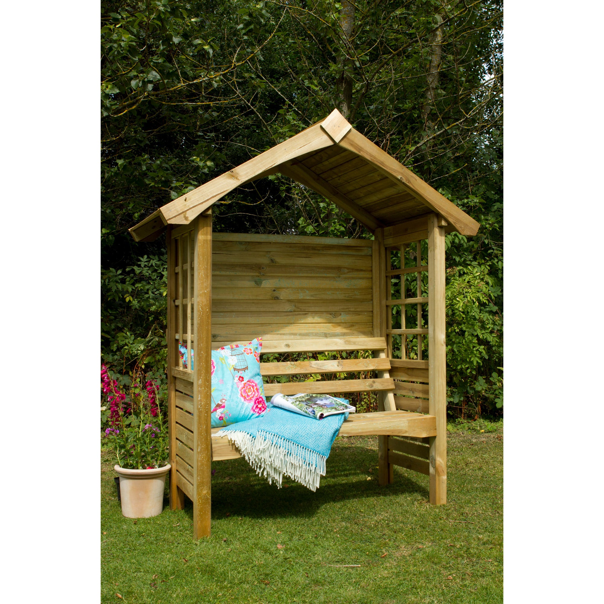 Wooden garden arbour seat with a slanted roof, featuring lattice side panels, a natural finish, and colorful cushions, set in a lush green garden.