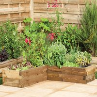A wooden corner raised bed in a natural brown finish, measuring 4'x4', filled with various green plants and herbs, set against a backdrop of a wooden fence and garden foliage.