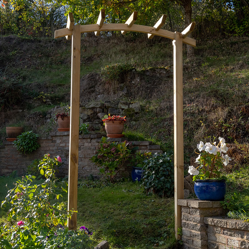 Wooden 4x2 pergola arch with a dome top, featuring a natural timber finish, decorative slats, and positioned in a garden with potted plants and flowers.
