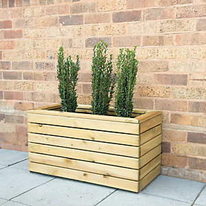 Wooden garden planter in a natural finish, featuring a rectangular design with horizontal slats, holding three green plants against a brick wall background.
