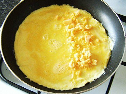 Two frying pans, one 20cm and one 24cm, featuring a black anti-stick coating, placed on a stove with an omelette cooking in the larger pan.