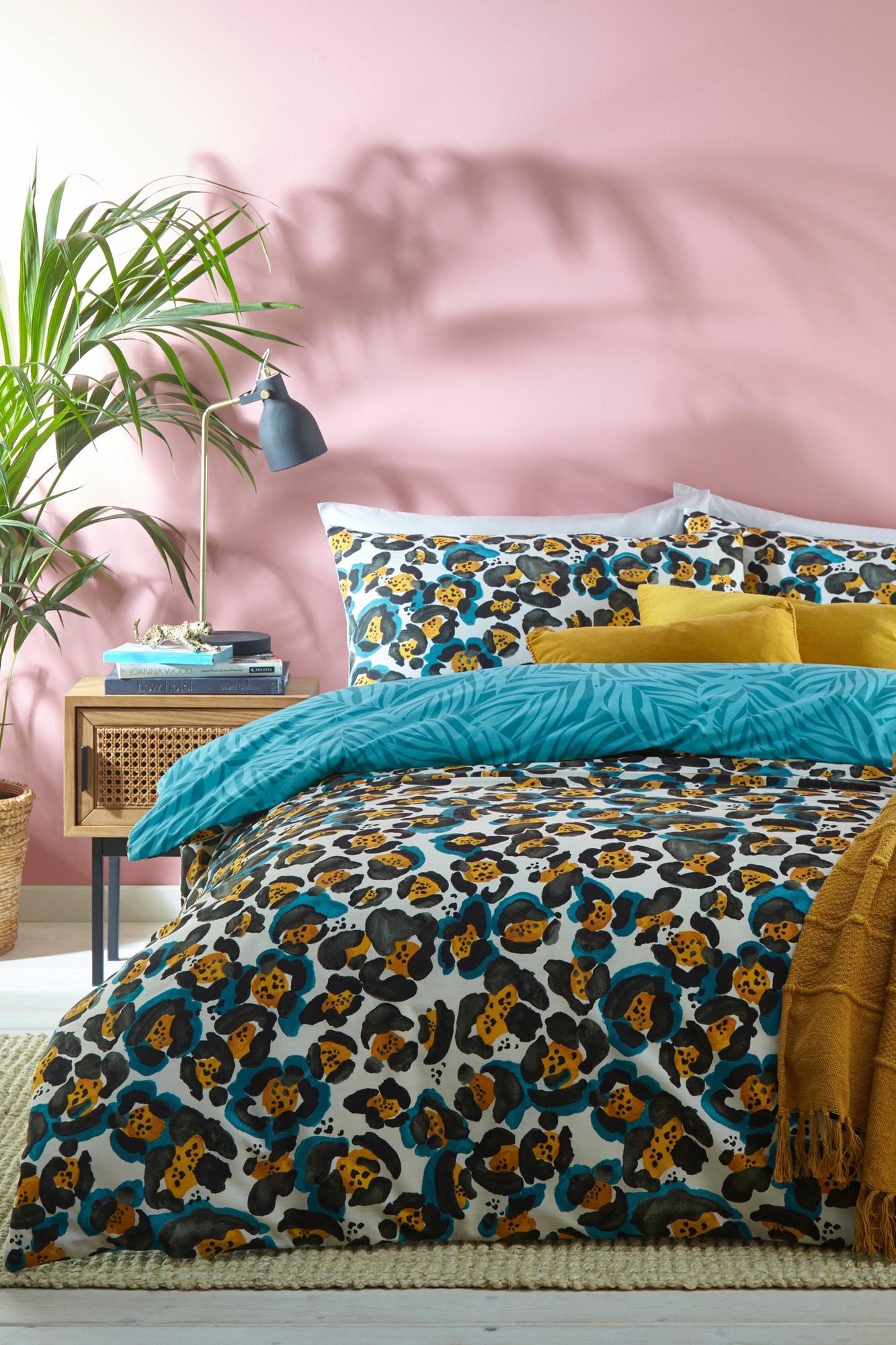Teal polycotton duvet cover set featuring a vibrant leopard print, complemented by yellow and teal accent pillows, styled in a cozy bedroom with a pink wall and a plant.
