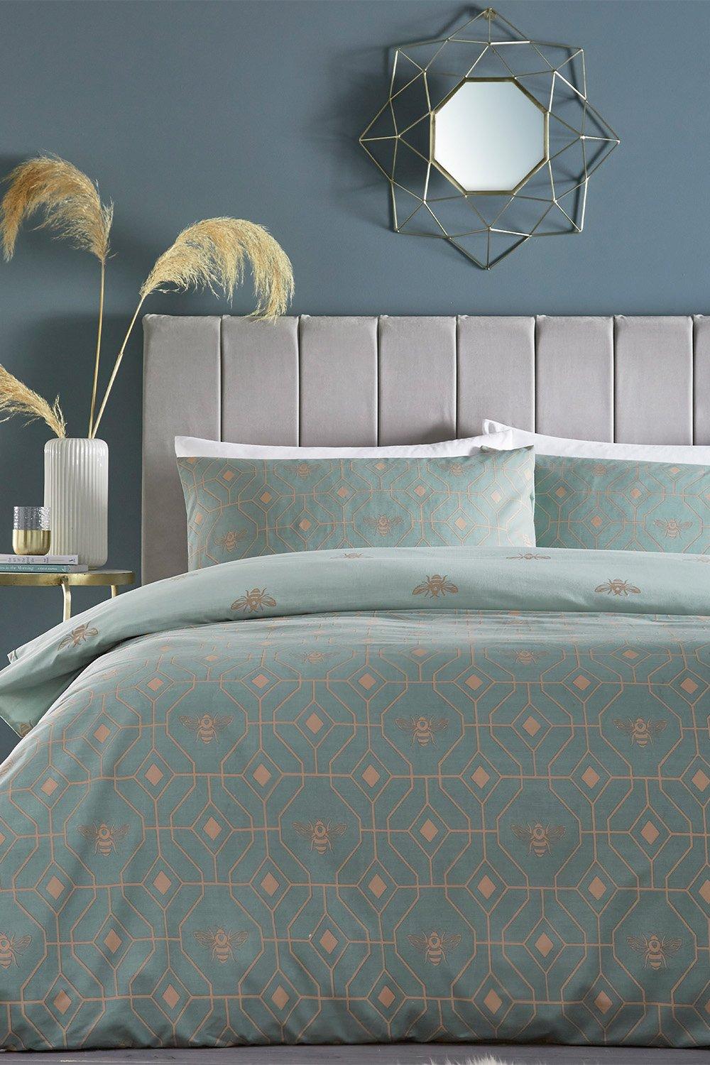 Light green geometric reversible duvet cover set with a subtle bee pattern, featuring matching pillowcases, set against a grey upholstered headboard and a decorative wall mirror.
