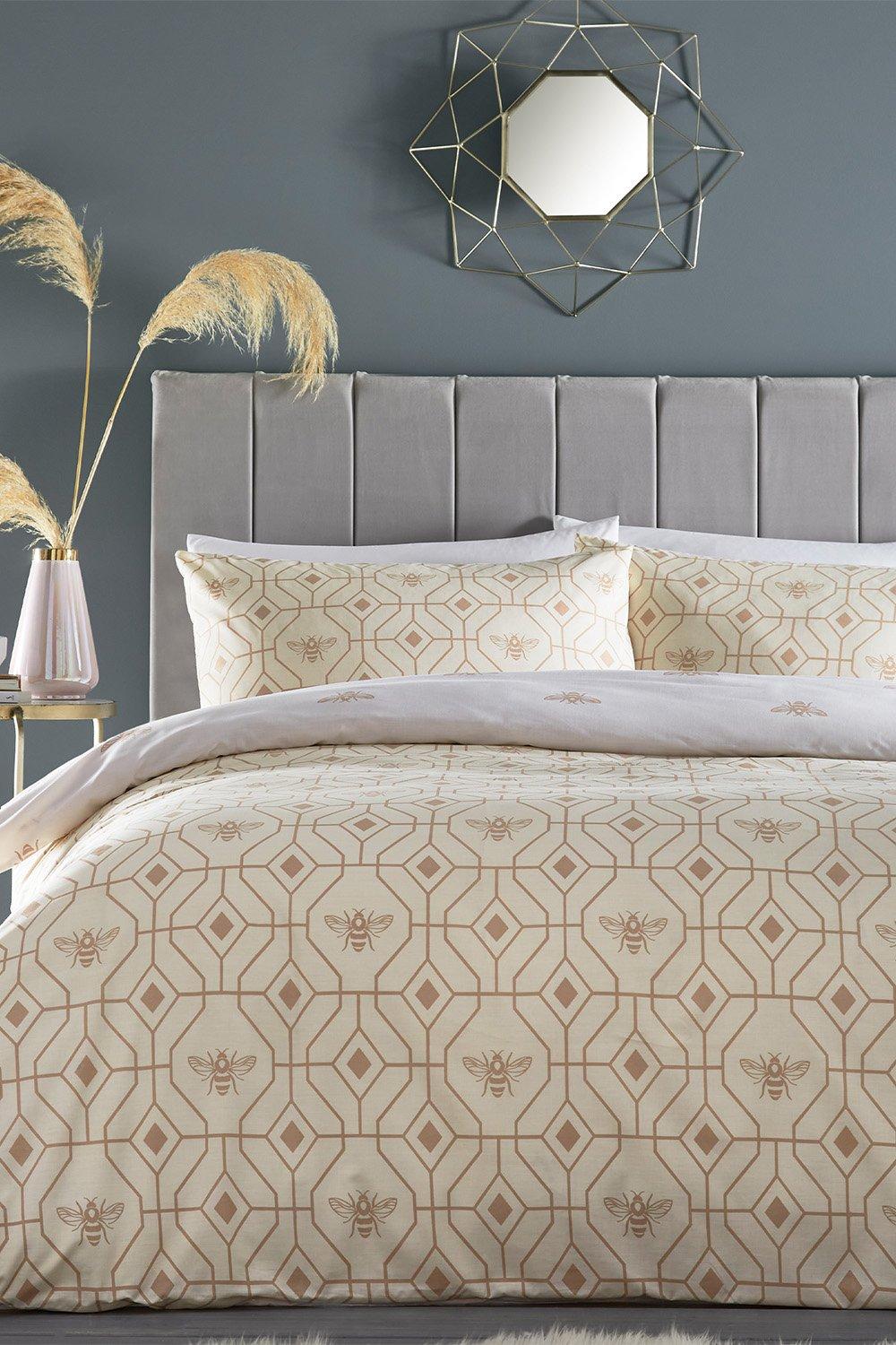 Champagne polycotton duvet cover set featuring a geometric bee pattern, complemented by matching pillowcases, displayed against a grey wall and stylish headboard.