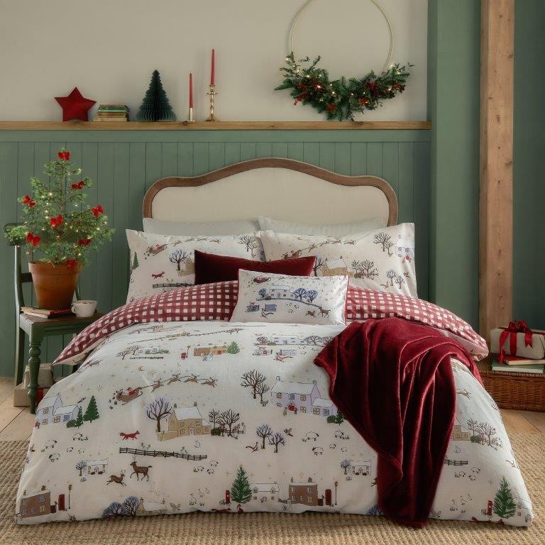 Reversible double duvet cover set featuring a festive Cotswolds Christmas print with quaint houses and trees, complemented by a red checkered cushion and a burgundy throw.