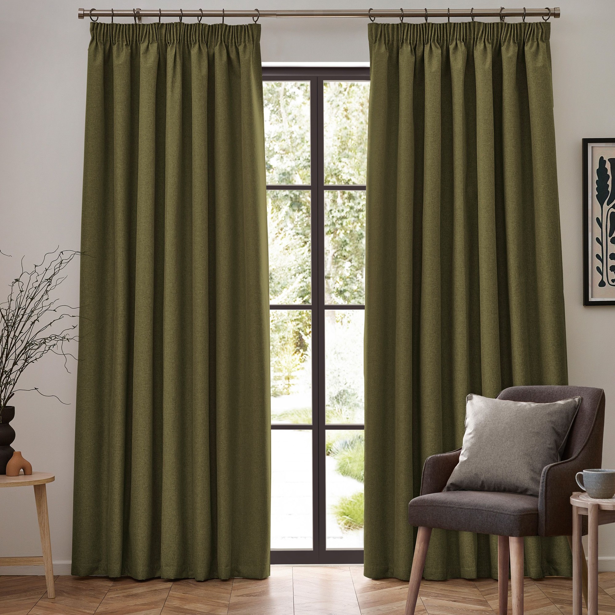 Olive green blackout pencil pleat curtain pair, measuring 168cm width by 137cm drop, hanging from a rod in a well-lit room with a plant and a chair.