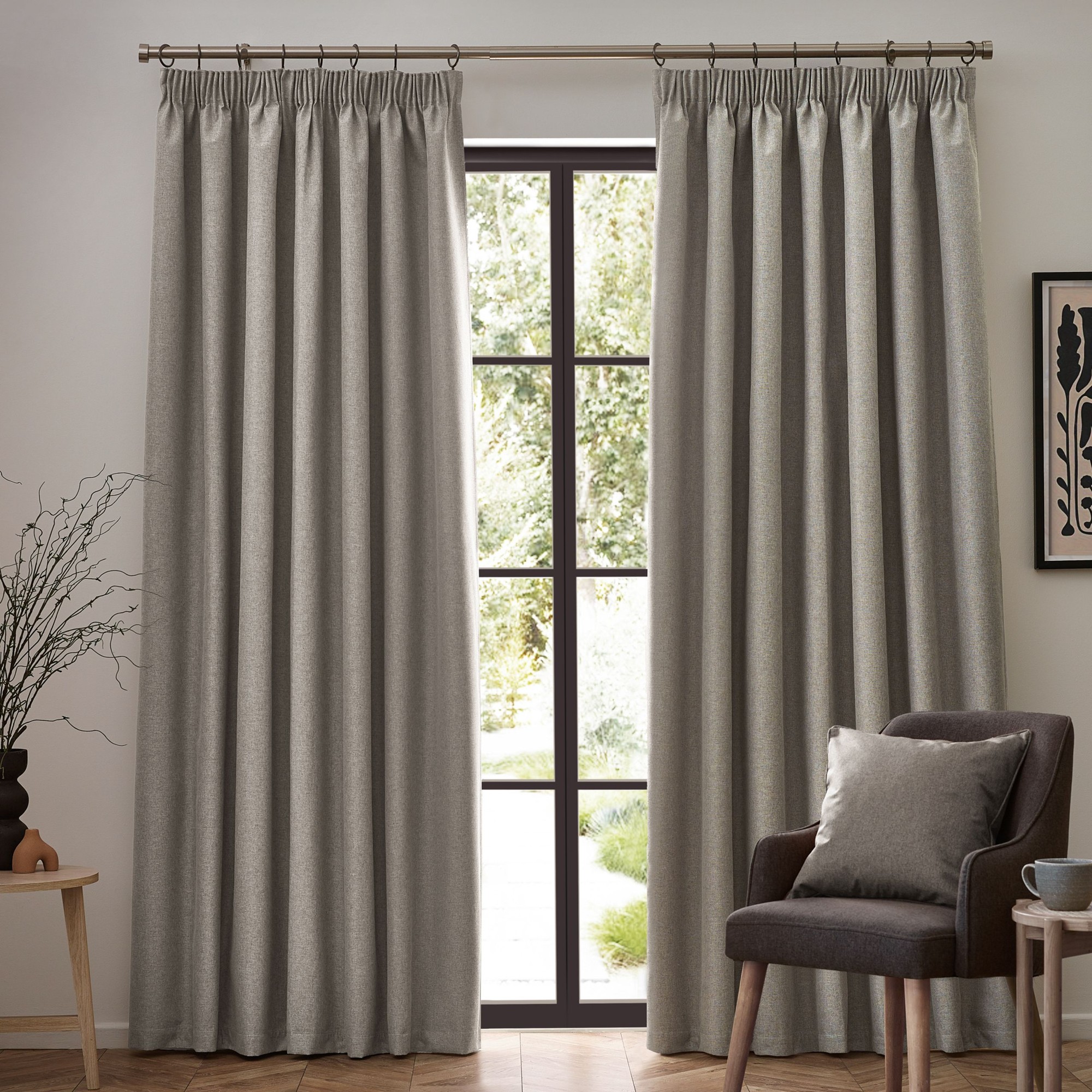 Beige blackout pencil pleat curtains with a textured finish, measuring 229cm wide by 183cm drop, elegantly framing a large window in a cozy room setting.