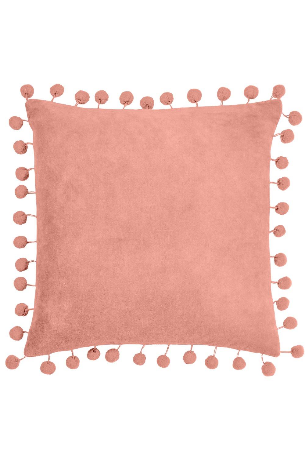 Square pink velvet cushion featuring a soft texture and decorative pom pom trim along the edges, adding a playful touch to home decor.