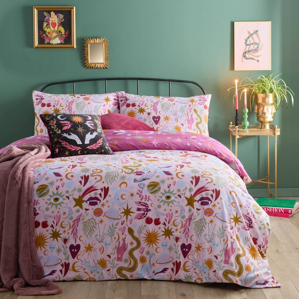 Reversible duvet set featuring a colorful, whimsical print with stars, eyes, and floral designs, complemented by pink and black cushions against a green wall.