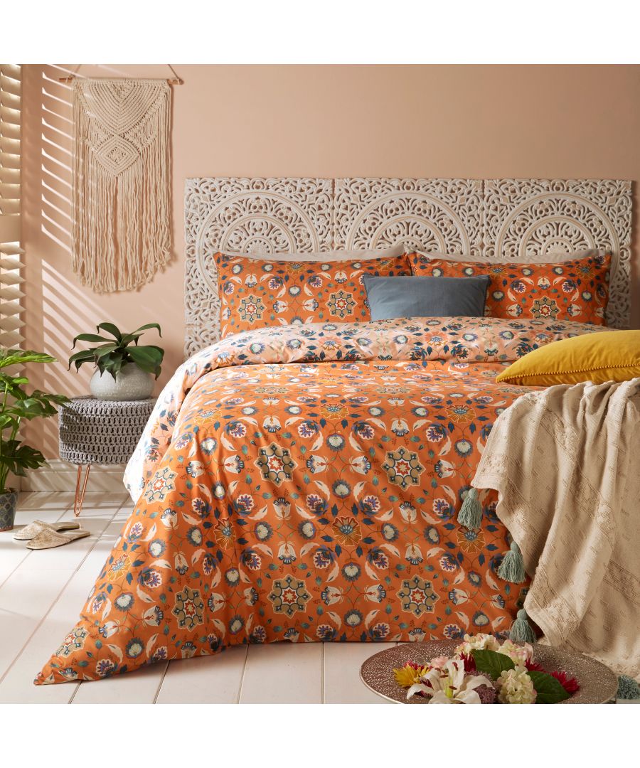 Orange cotton duvet cover set featuring a floral pattern, complemented by blue and yellow accent pillows, set against a light wall and decorative wall hanging.