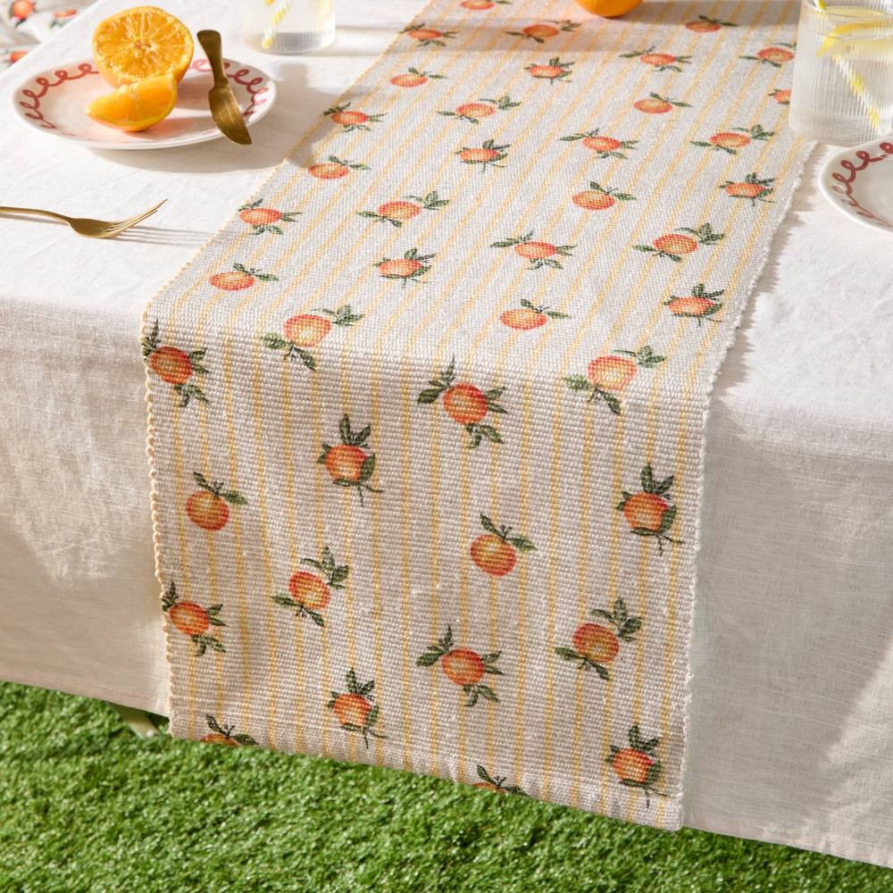 Cream table runner featuring a fruit pattern of small oranges on a striped background, measuring 220 x 35 cm, suitable for indoor or outdoor use.