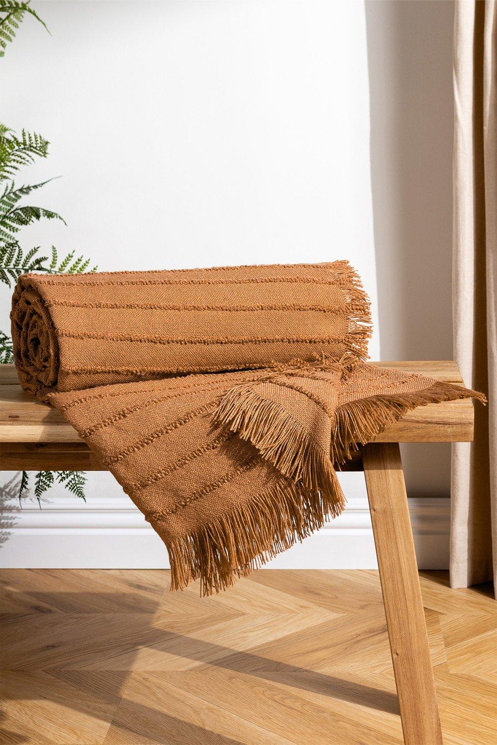 Brown linear yarn woven throw with fringed edges, rolled and placed on a wooden bench, featuring textured stripes and a warm, cozy appearance.