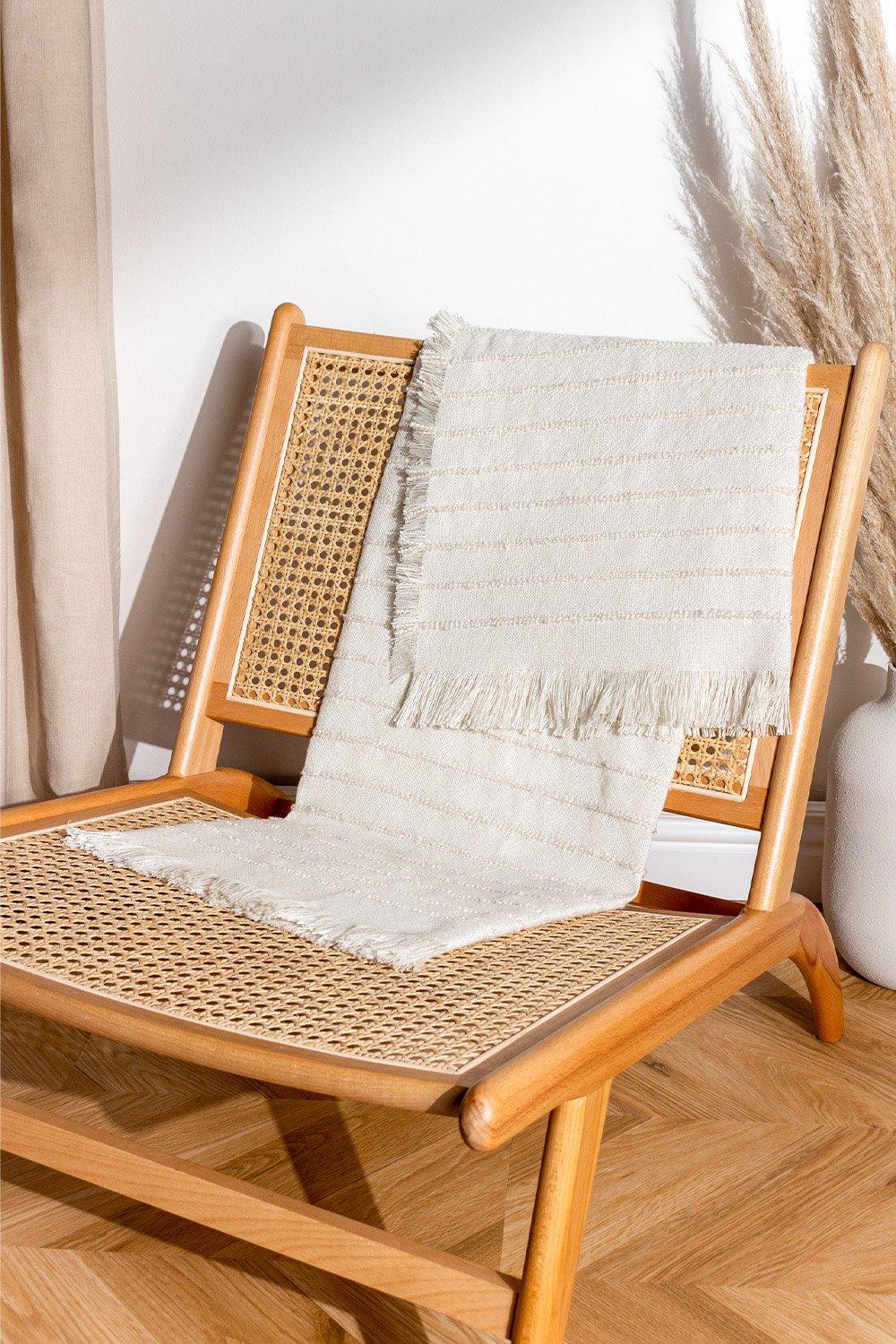 Natural-colored yarn woven throw with fringed edges draped over a wooden chair, featuring a textured pattern and soft, cozy appearance.