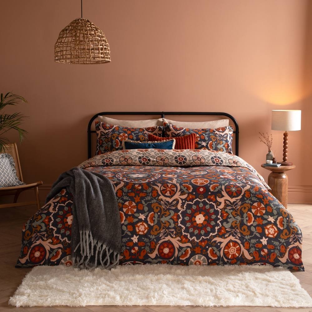 Kinfolk Floral Duvet Cover Set in blue, featuring intricate floral patterns in warm hues, complemented by a cozy gray throw and styled on a black metal bed frame against a warm-toned wall.