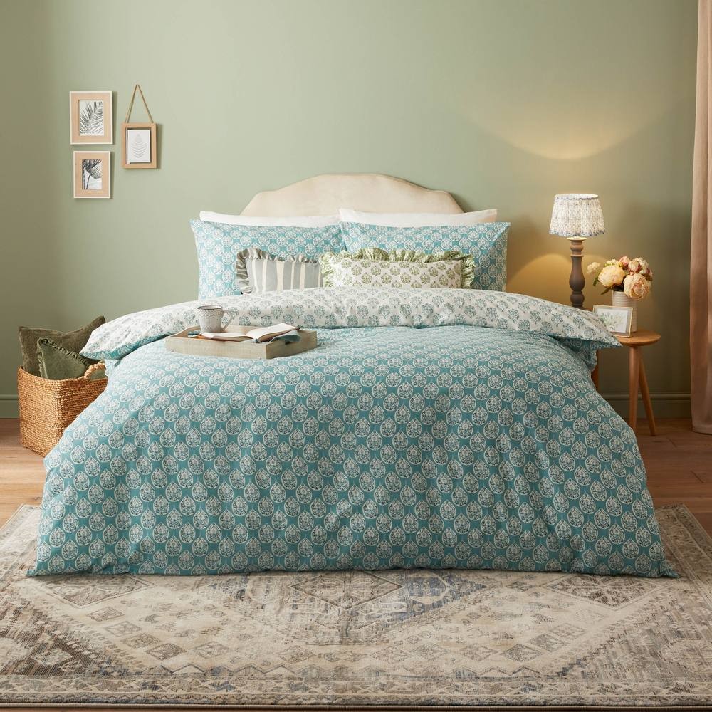Blue block printed duvet cover set featuring intricate white floral patterns, complemented by matching pillowcases, styled on a cozy bed with decorative cushions and a soft rug.