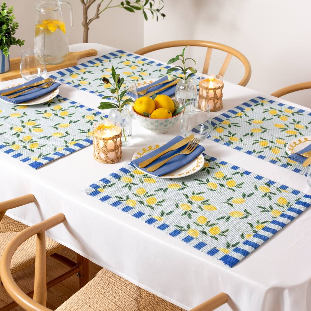 Set of four blue placemats featuring a lemon pattern, made for indoor/outdoor use, arranged on a white tablecloth with tableware and decorative elements.