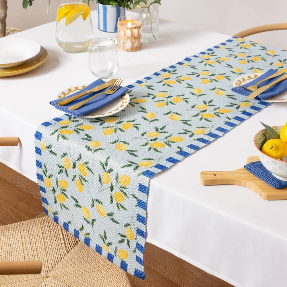 Large blue table runner featuring a lemon pattern, made of durable material, with a striped border, placed on a white table with decorative dishes and a pitcher.