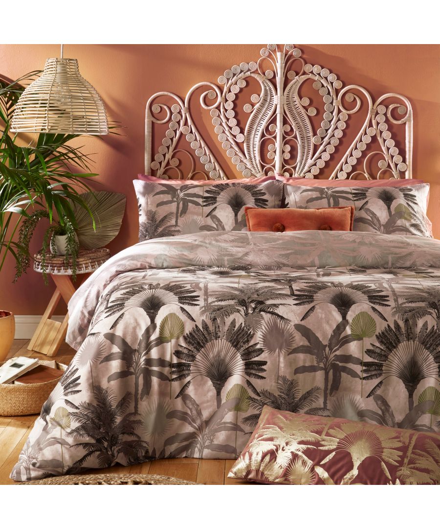 Blush cotton duvet cover set featuring a tropical palm print, complemented by matching pillowcases and a decorative cushion, set against a warm-toned wall and woven decor.