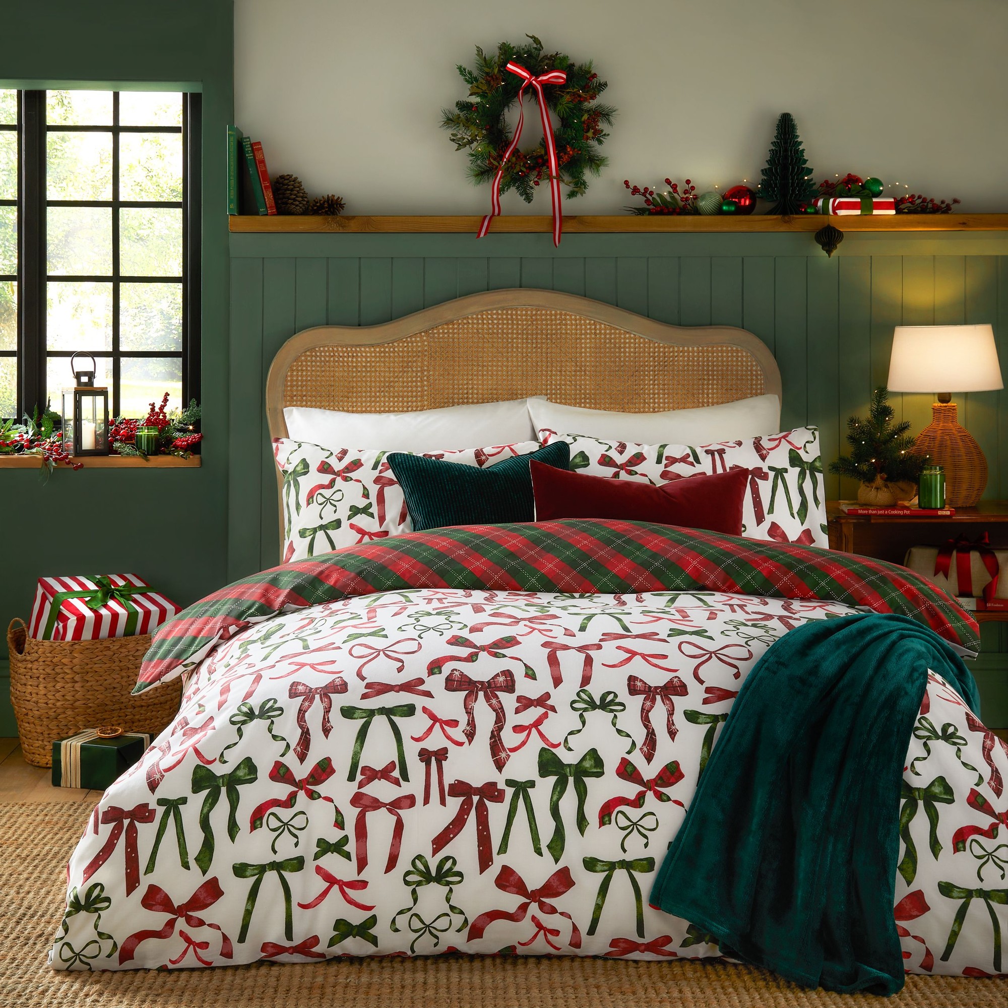 Festive duvet cover set featuring vibrant red and green bows on a white background, complemented by plaid and solid color pillows, set against a cozy, holiday-themed bedroom backdrop.