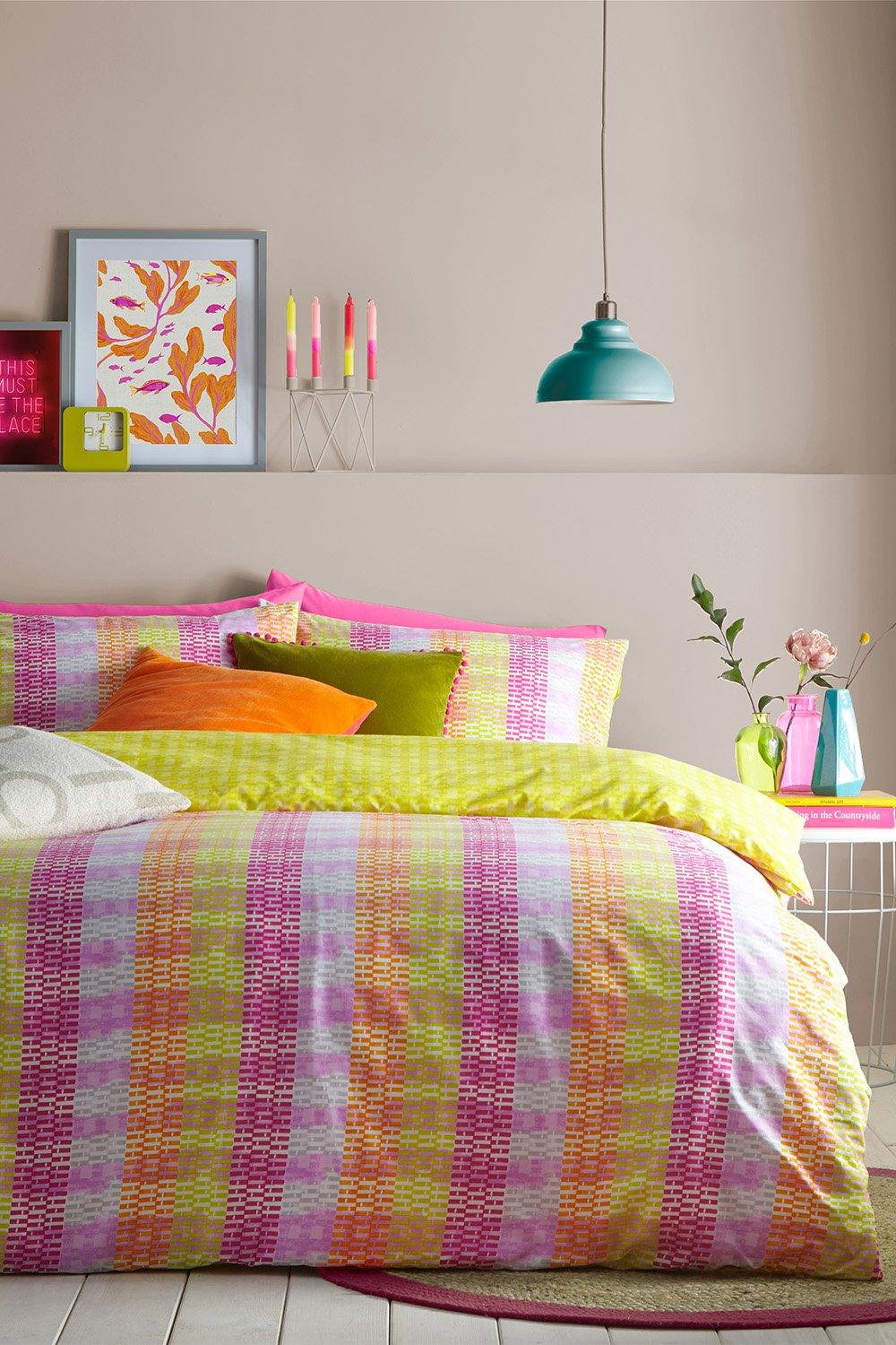 Multicolour striped reversible duvet cover set in polycotton, featuring vibrant pink, green, and orange hues, styled with decorative cushions and a modern lamp.