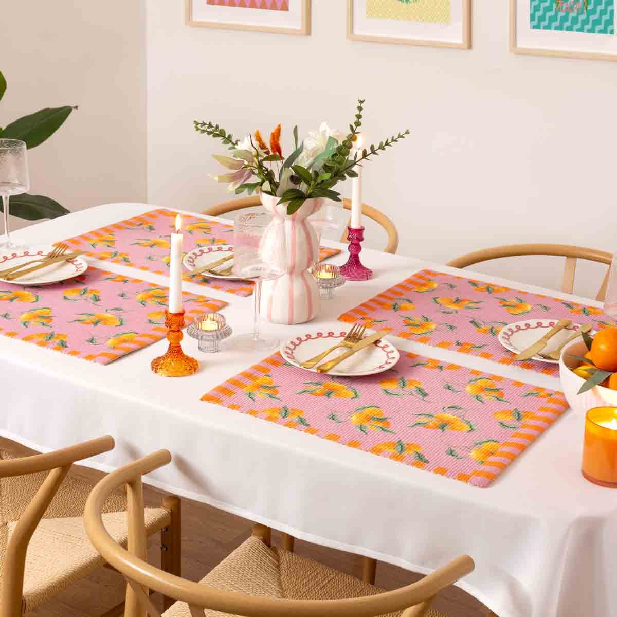 Set of 4 pink indoor/outdoor placemats featuring vibrant orange fruit designs, made from durable material, arranged on a dining table with decorative candles and flowers.
