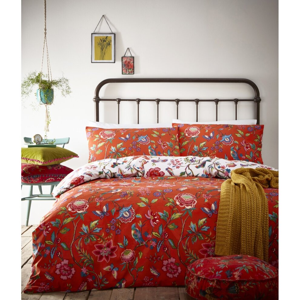 Vibrant orange double duvet set featuring intricate floral and bird patterns, complemented by matching pillowcases and a cozy mustard throw on a rustic wooden bed frame.