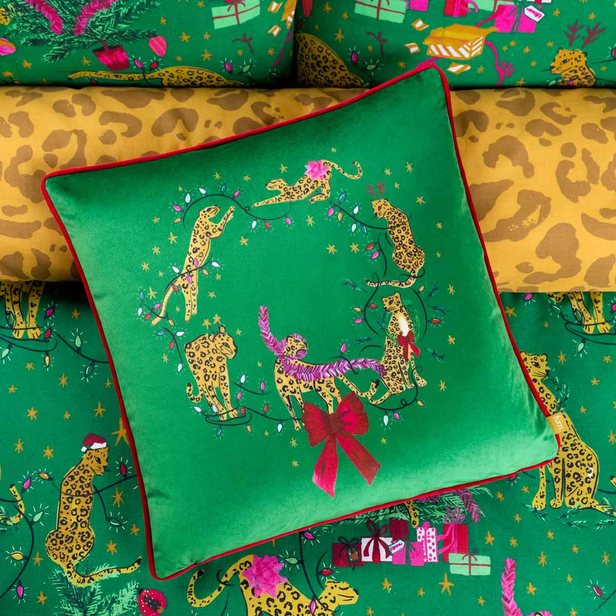 Bright green velvet cushion featuring leaping leopards in vibrant colors, adorned with festive decorations and a red piped edge, measuring 43cm x 43cm.