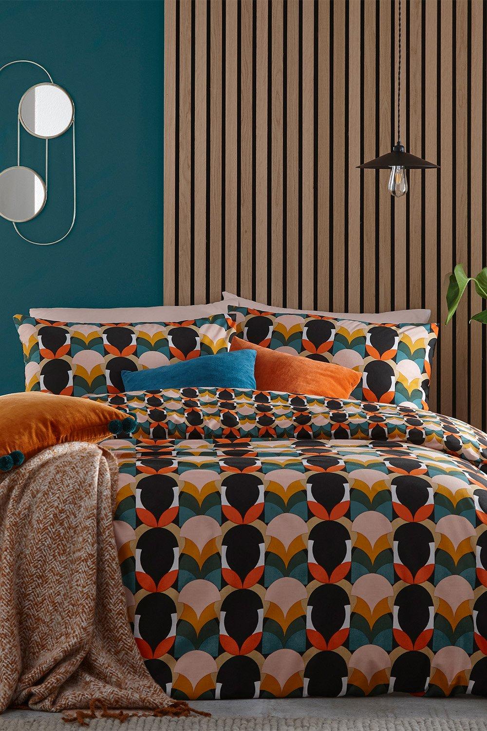 Multi-colored Art Deco duvet set featuring bold geometric patterns in orange, teal, and black, complemented by vibrant pillows and a textured throw against a wooden panel backdrop.