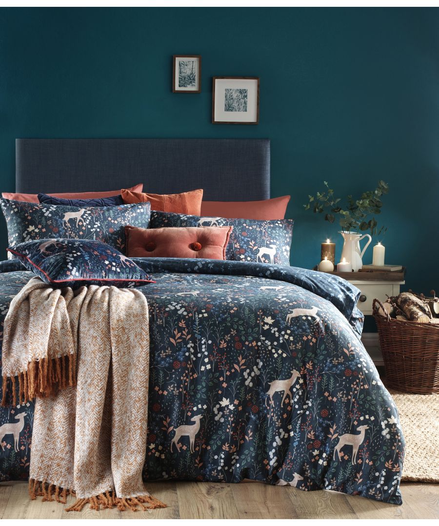 Richmond duvet set in midnight blue cotton features a floral and deer print, complemented by textured cushions and a cozy throw, set against a dark teal wall.