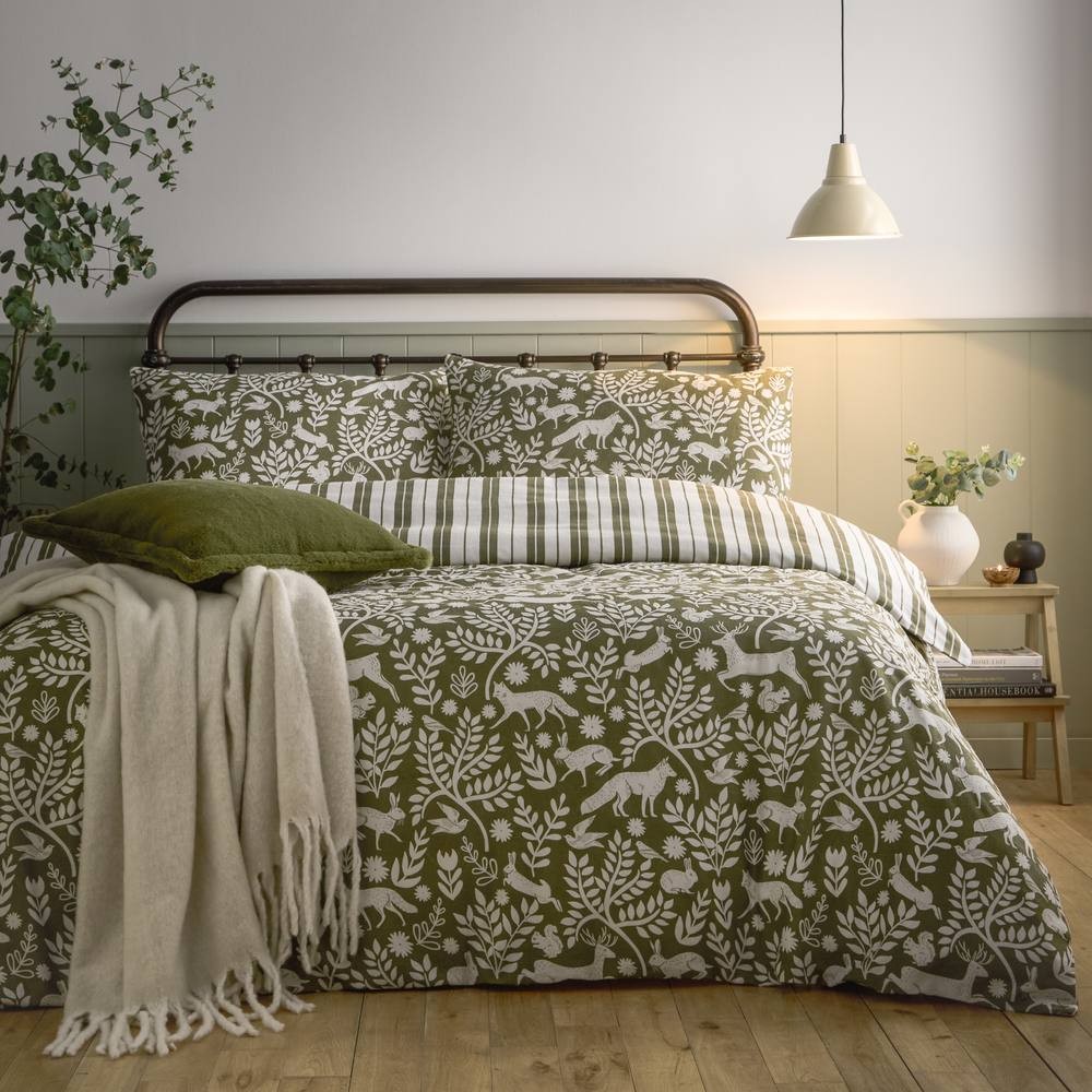 Green brushed cotton duvet cover set featuring woodland animal and foliage patterns, complemented by striped pillowcases and a cozy cream throw on a wooden bed frame.
