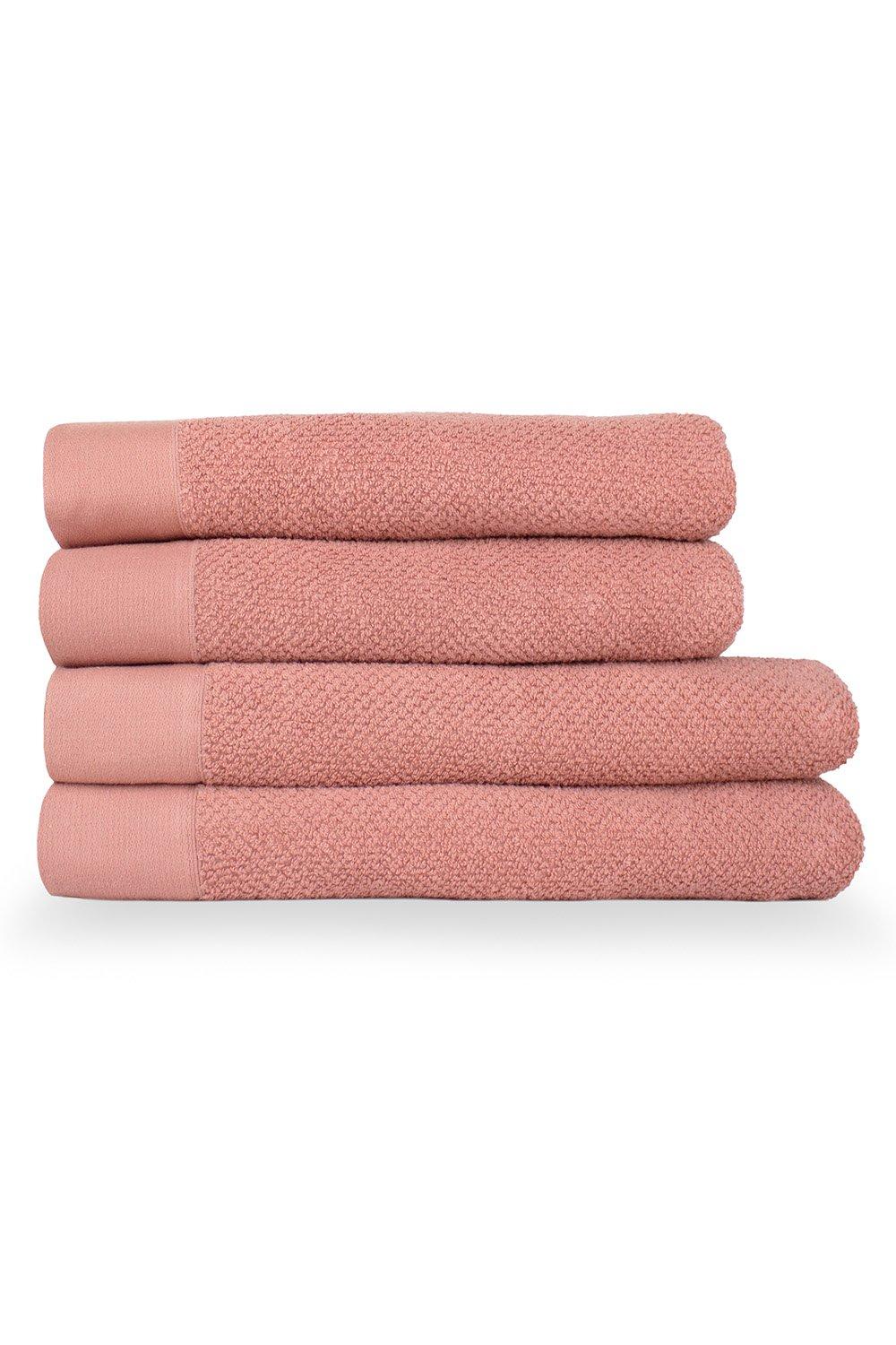 Four stacked bath towels in a soft pink hue, featuring a textured weave design, made from cotton with a plush, absorbent finish.