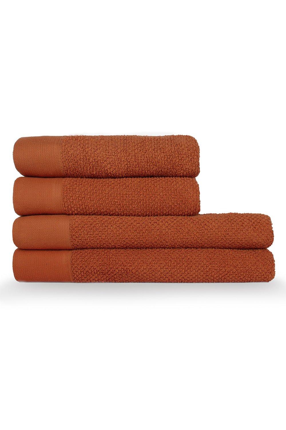 Four stacked towels in a warm terracotta color, featuring a textured weave and a soft, absorbent cotton material, ideal for hand and bath use.