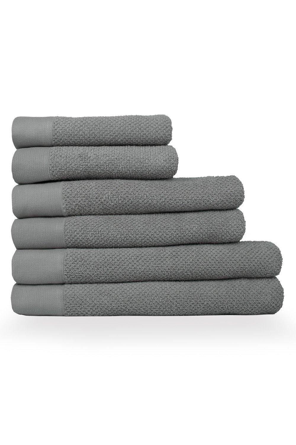 Six stacked towels in a soft gray color, featuring a textured weave design with a smooth cotton finish, suitable for hand, bath, and sheet use.