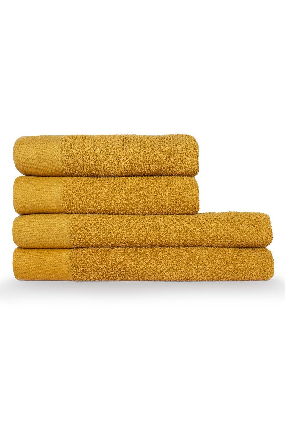 Four stacked towels in a warm mustard yellow, featuring a textured weave and contrasting smooth cotton panel at the ends, ideal for hand or bath use.