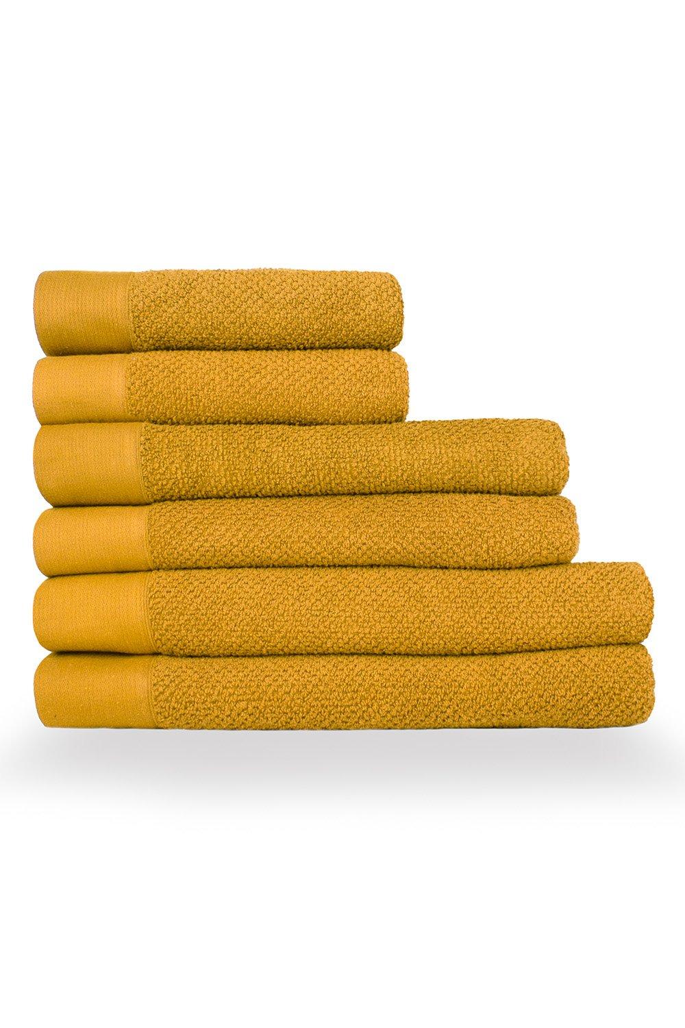 Six stacked towels in a rich mustard yellow, featuring a textured weave and a soft cotton material, ideal for hand, bath, and sheet use.