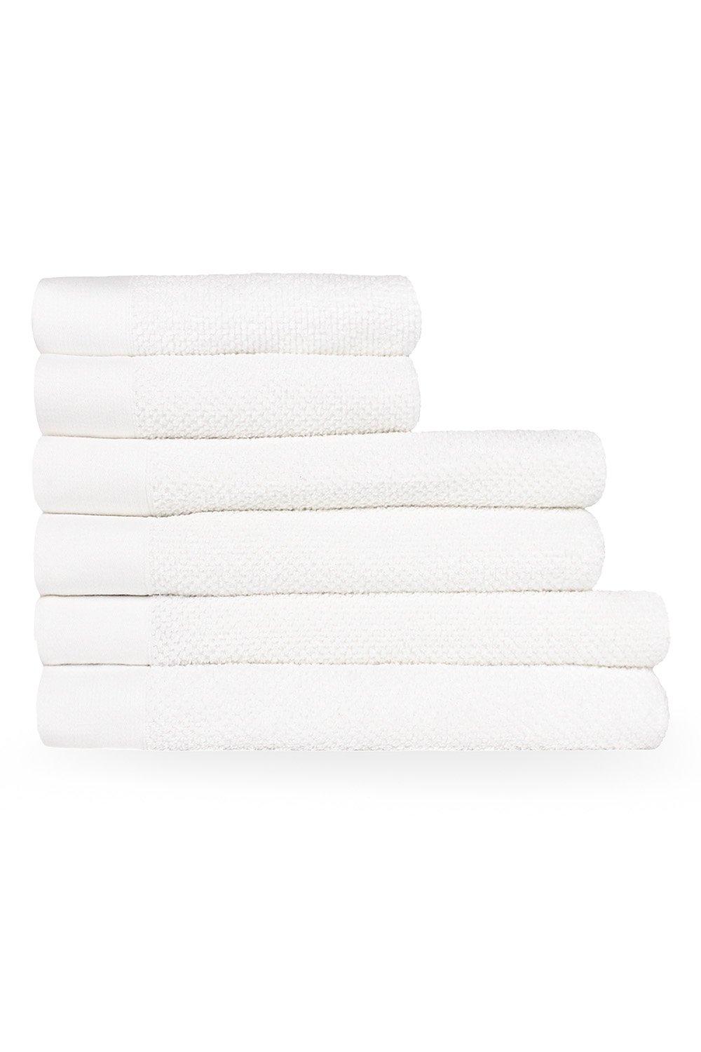 Six white cotton towels are neatly stacked, featuring a textured weave design, ideal for hand, bath, and sheet use.
