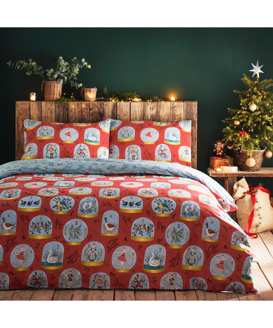 Festive reversible duvet cover set in red featuring Christmas-themed illustrations, paired with matching pillowcases, displayed on a wooden bed against a dark green wall and decorated Christmas tree.