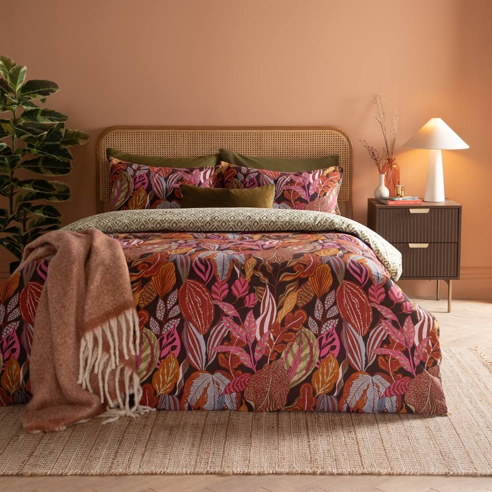 Reversible super king duvet cover set featuring vibrant floral and leaf prints in warm tones, complemented by matching pillowcases and a cozy throw blanket on a textured bed.