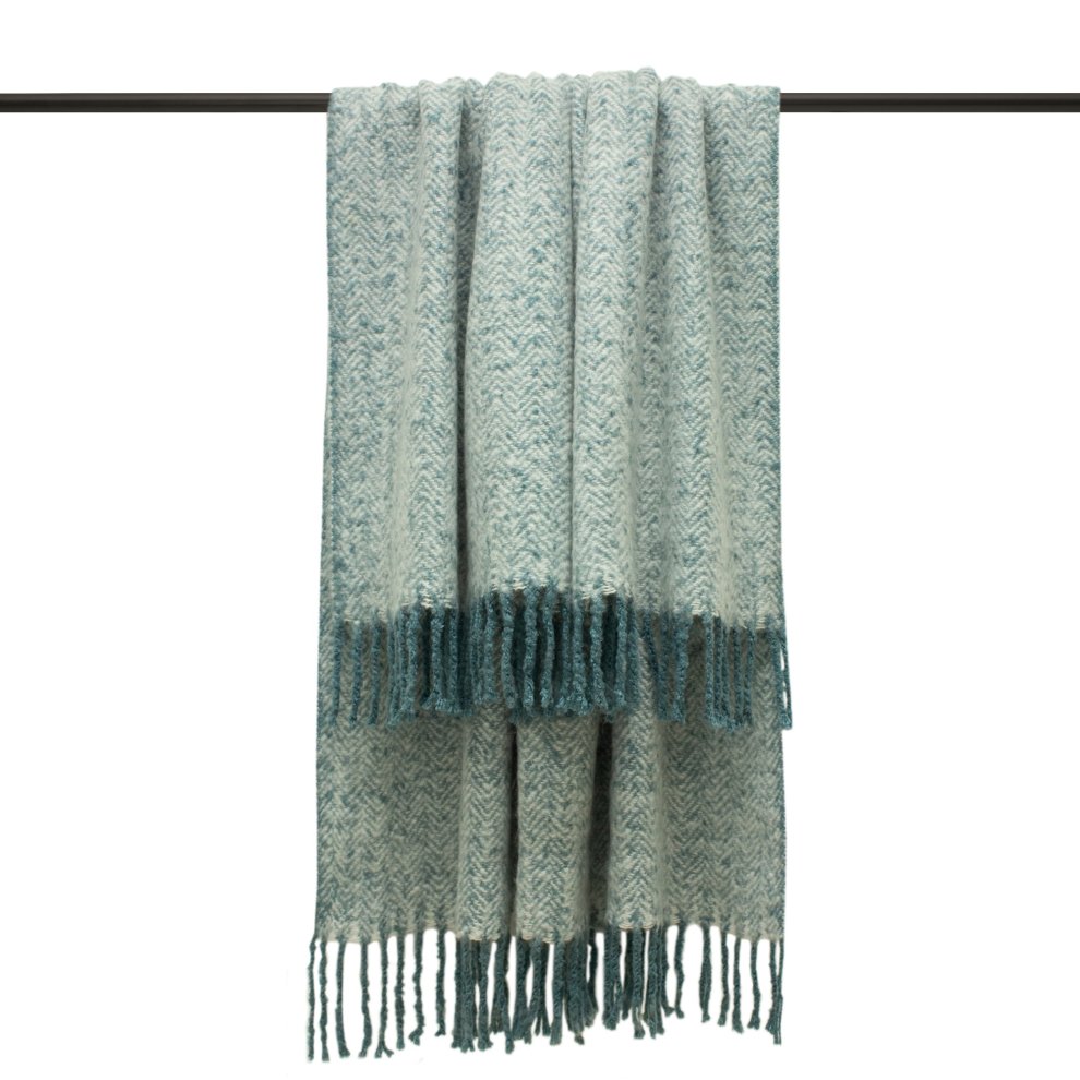 Teal woven herringbone throw blanket with fringed edges, featuring a soft texture and a stylish pattern, hanging from a rod.